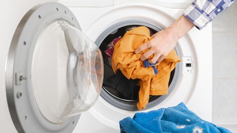 Mão a colocar peças de roupa colorida dentro do tambor da máquina de lavar roupa.